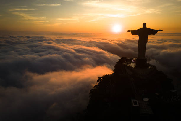 Rio de Janeiro, Brazil - April 11, 2024: Dramatic view of Christ the Redeemer statue on top of the Corcovado mountain above clouds during sunrise.