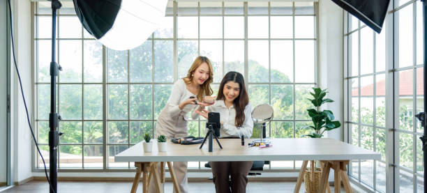istock Two asian women creating content for social media. They are using a studio setup that include a smartphone mounted on a tripod, lighting equipment, and various makeup products arrayed on the table. 2151881700