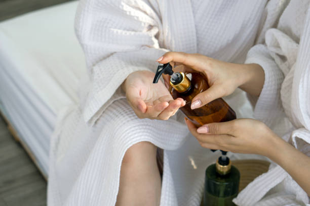 istock Two women in white robe dispensing a liquid from a brown bottle into their hand. 2151881701