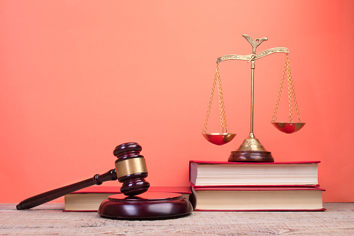 Law concept - Open law book, Judge's gavel, scales, Themis statue on table in a courtroom or law enforcement office. Wooden table, red background.
