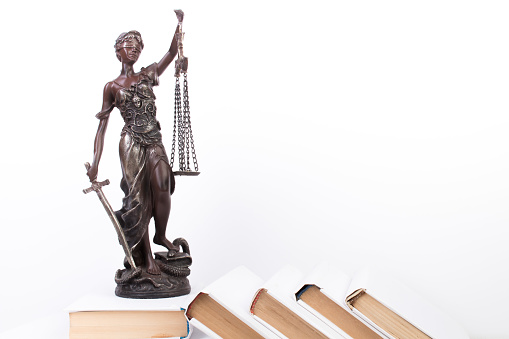 Law concept - Open law book, Judge's gavel, scales, Themis statue on table in a courtroom or law enforcement office. Wooden table, white background