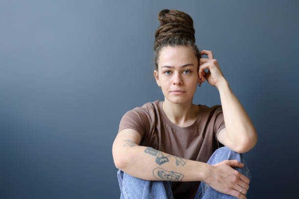 istock Tattooed Woman with Dreadlocks in Bun Sitting on Grey 2151883959