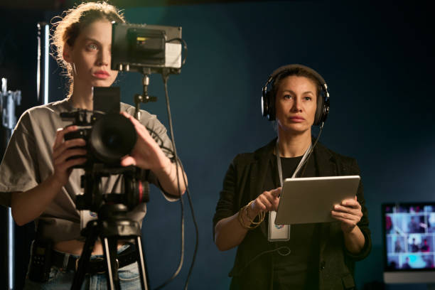 Waist up portrait of two women working in video production crew and operating camera on set