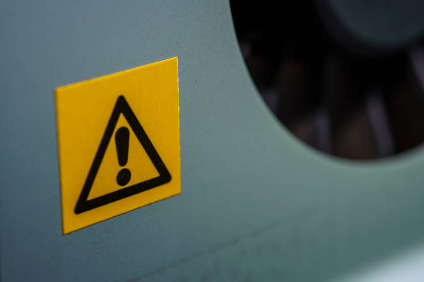 Yellow and black warning label with an exclamation mark. It is affixed to machinery and serves as a safety alert. The label signifies potential hazards, urging caution and vigilance