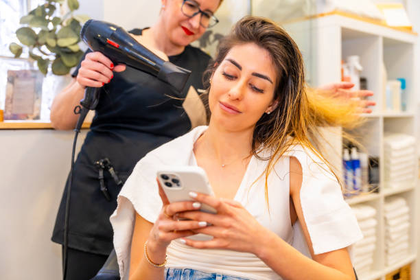 istock Client using phone while hairdresser drying her hair 2151886385