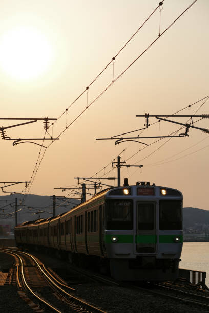 Otaru-city, Hokkaido, Japan - May 4, 2024 : 721 Series Rapid train “Airport” running along the shoreline at sunset