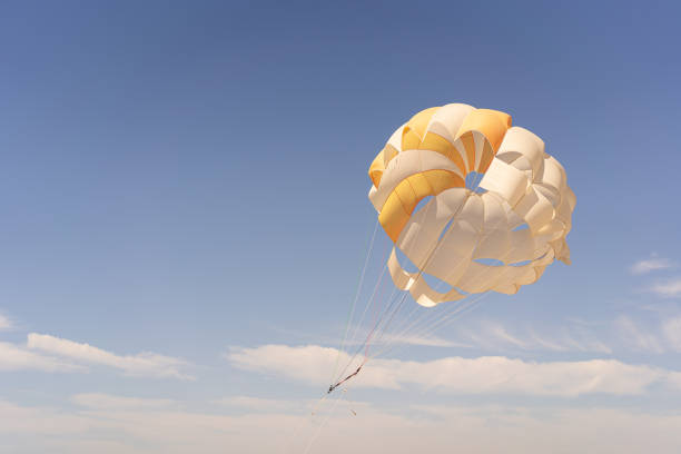 The parachute is fully inflated, showcasing vivid yellow and white colors as it glides through the air.