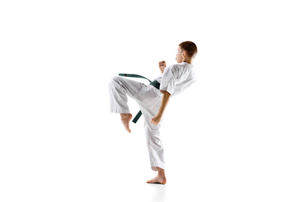 Karate student in white kimono and green belt, in motion, performing powerful kick during practice session, isolated on white background. Concept of sport, martial arts, combat sport, active lifestyle