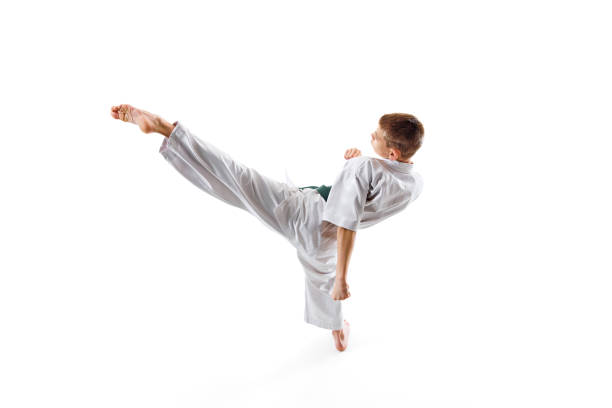 Martial arts training session capturing young athlete high kick, teen boy practicing isolated on white studio background. Concept of sport, martial arts, combat sport, healthy and active lifestyle