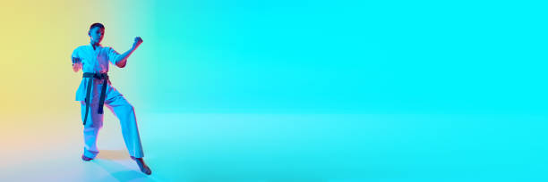 istock Athletic young martial artist in a kata position, demonstrating focus and concentration against gradient orange blue background in neon light 2151899115