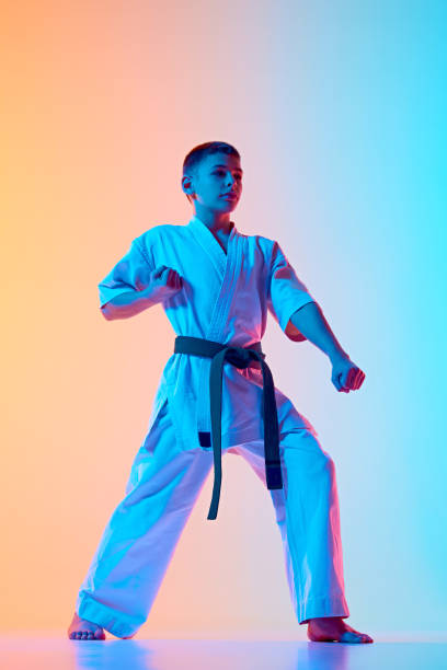 istock Young karateka in a defensive posture, teen boy practicing against gradient orange blue background in neon light 2151899121