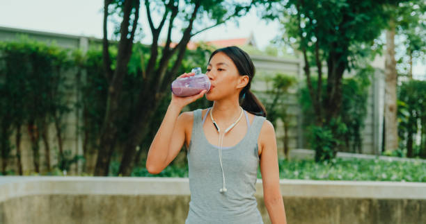 istock Young Asian female athlete runner drinking protein shake after exercise workout in urban park. Diet and healthy food workout exercise. 2151903566