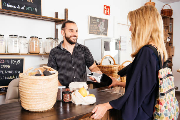 istock Smiling Cashier Accepting Smartphone Payment at a Rustic Grocery Counter 2151903800