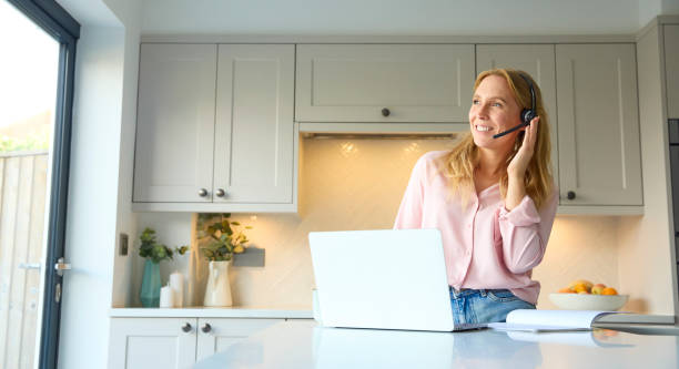 istock Woman Wearing Headset Working From Home In Kitchen Using Laptop 2151907601