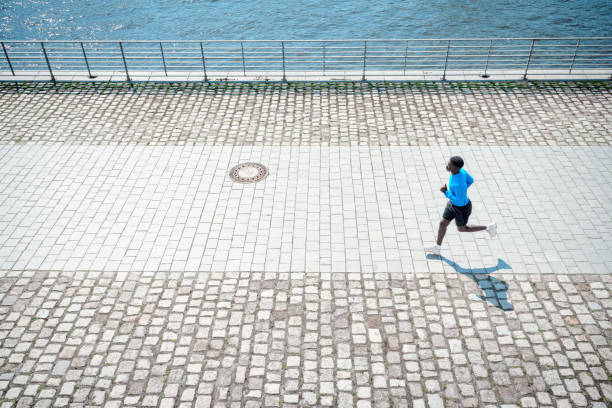high angle view on young black sportsman running  alongside river in berlin city at sunny day