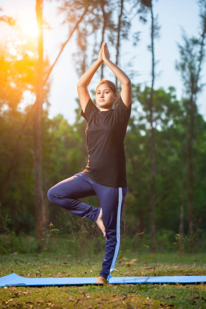 istock women doing Vrksasana or tree pose during sunrise at park 2151920063
