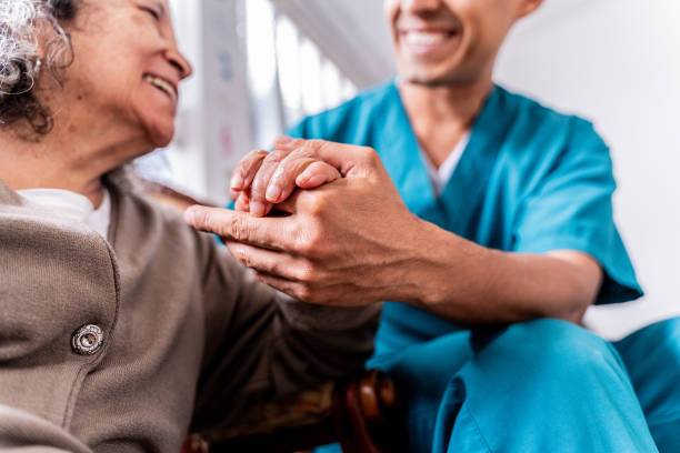 senior woman holding caregiver's hands at home - ouderenzorg stockfoto's en -beelden