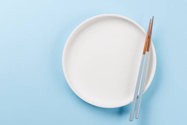Asian culinary table setting featuring a nested bowl and plate with blue floral design, black chopsticks, and a red chili pepper rest