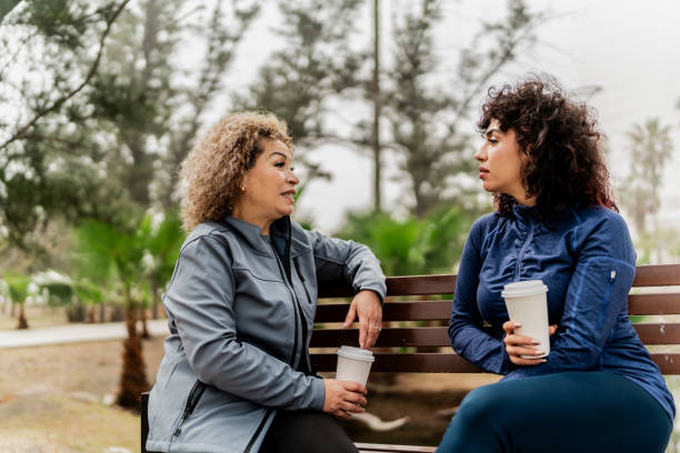 Mother and daughter talking sitting on park bench at public park