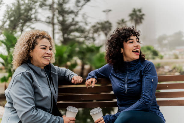 istock Mother and daughter talking sitting on park bench at public park 2151931446