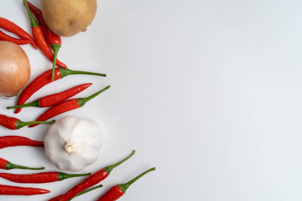 Layflat composition featuring vibrant red chili peppers, garlic, and onions with acopy space against a clean, white backdrop.