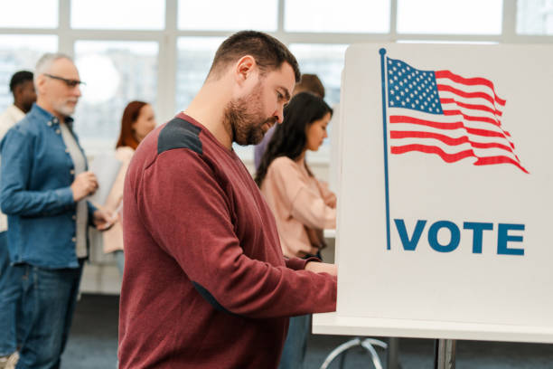 istock Attractive, middle aged man standing in voting booth with American flag, voting at polling station 2151940252