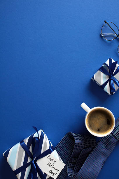 istock Happy Fathers Day vertical banner design. Flat lay gift boxes, coffee cup, glasses, necktie on dark blue background. 2151941333