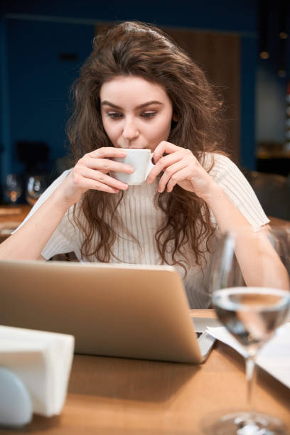 istock Cute woman drinks coffee in a restaurant using a laptop 2151948832