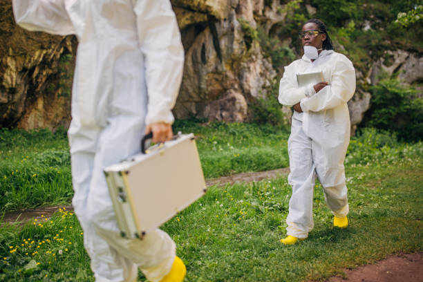 Two environmental scientists in protective suits carrying out conservation research in a natural, outdoor setting with equipment and documentation