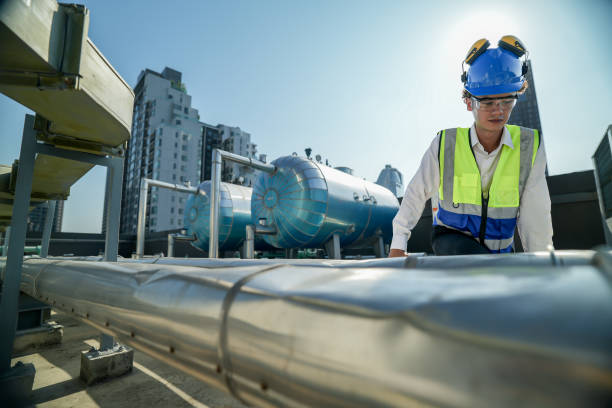istock Serious engineer inspecting HVAC equipment with a tablet on a commercial building rooftop. A focused engineer wearing a safety helmet and vest inspects machinery on a city building’s rooftop. 2151959825