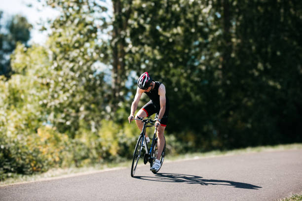 A male triathlete begins a ride while doing a cycling training session along a rural paved bike path on a sunny day in Washington state.