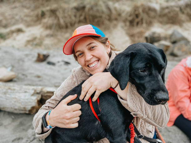 istock Woman smiles while sitting with her dog on the beach 2151964281