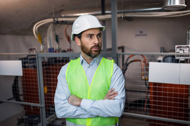 istock male engineer technician standing in technical room of electrical switchboard, wearing green safety vest, helmet in environment of electrical substation. 2151968979