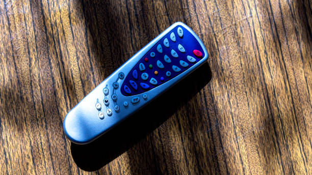istock Close up of old TV remote control on table surface, light creates contrasting shadows on textured wooden background 2151969059