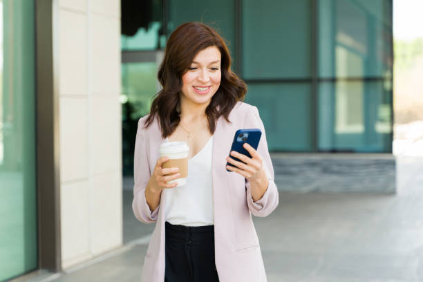 istock Female professional multitasking with a smile, texting on smartphone and holding coffee while walking in the city 2151973441