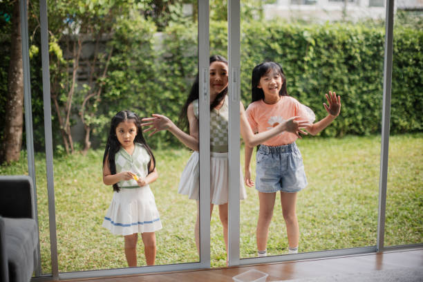 Smiling girls are looking through the window from outside the house.