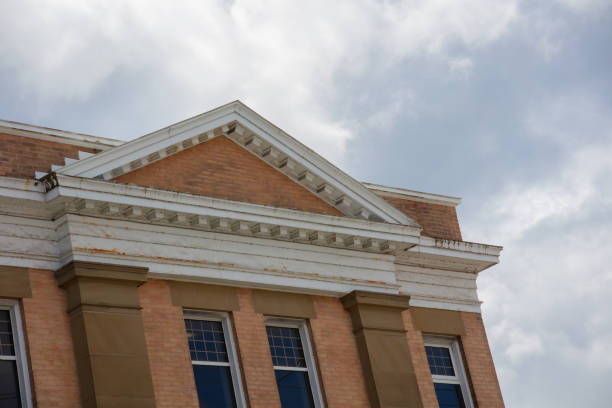 Charming old building boasts decorative beige brick cornice and triangle roof against a cloudy sky.