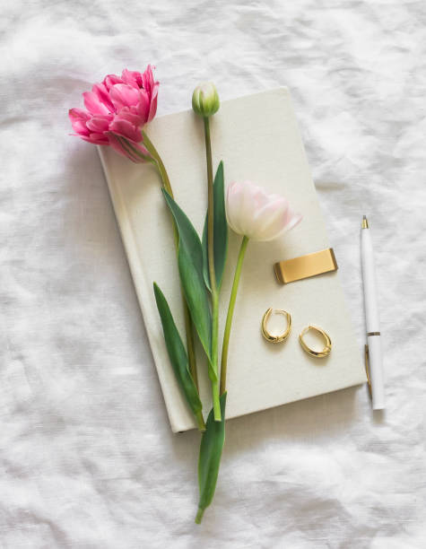 istock Tulips, a book, earrings, a pen on white sheets top view. Aesthetic still life 2151980090