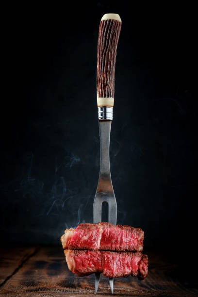 istock Fork with sliced grilled beef fillet steak on a wooden table, rare roasting 2151980982