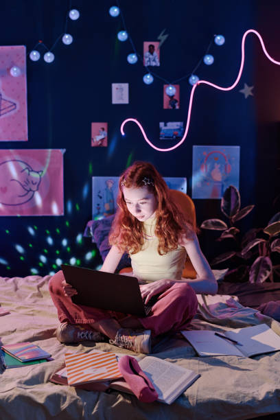 istock Girl Sitting On Bed Doing Homework on Laptop In Evening 2151989248