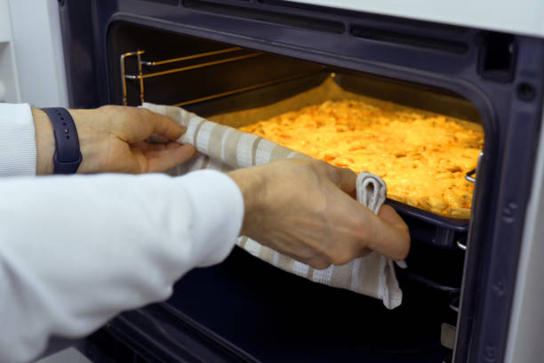 A man wearing oven mitts pulls a tray of freshly baked vegetarian pizza out of a hot oven as steam rises.
