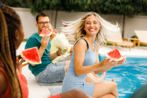 Carefree woman having fun on a party with her friends. Cheerful woman having fun while eating watermelon with her friends on a party by the pool. black man eating watermelon stock pictures, royalty-free photos & images
