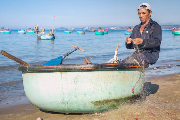 Vietnamese man checking fishing nets, fishing village, Mui Ne, Vietnam. Fishermen's boats on the background.