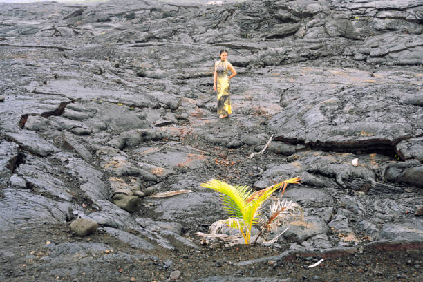 Woman in yellow dress walking in the back of green coconut young tree that growing on black lava volcano rocks.