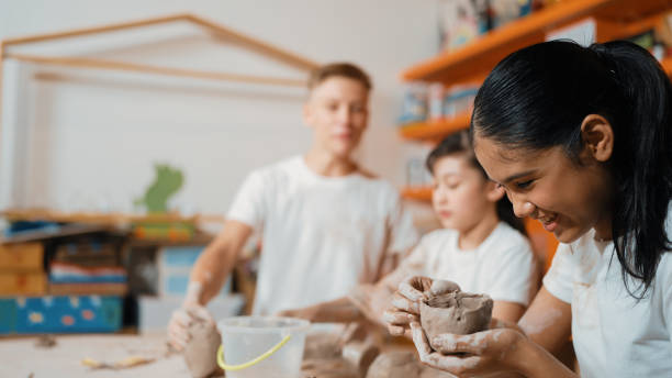 istock Boy modeling bowl of clay while cute asian girl working on dough. Edification. 2152000783