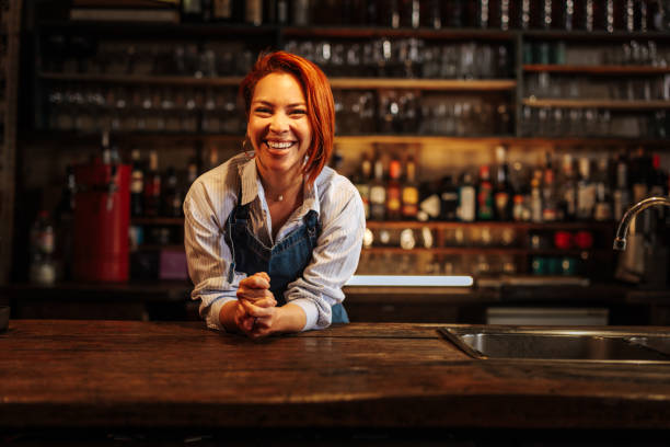 istock Female bartender leaning on a counter and laughing in a bar. 2152001442