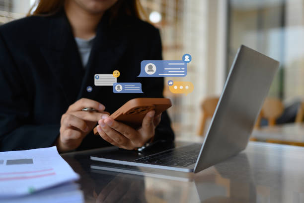 istock Young female worker using mobile phone with notification icons commenting in online community 2152001809