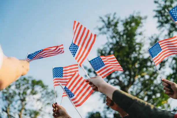 A group of people is waving small American flags at sunset A group of people is waving small American flags at sunset