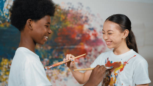 istock Smiling diverse children paint color on each other shirt at wall. Edification. 2152005982