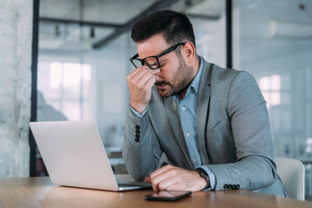 Stressed businessman having headache while working on laptop in the office.